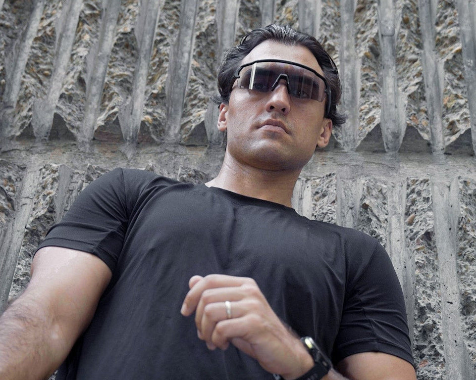 Man in black athletic wear and running sunglasses against a textured wall